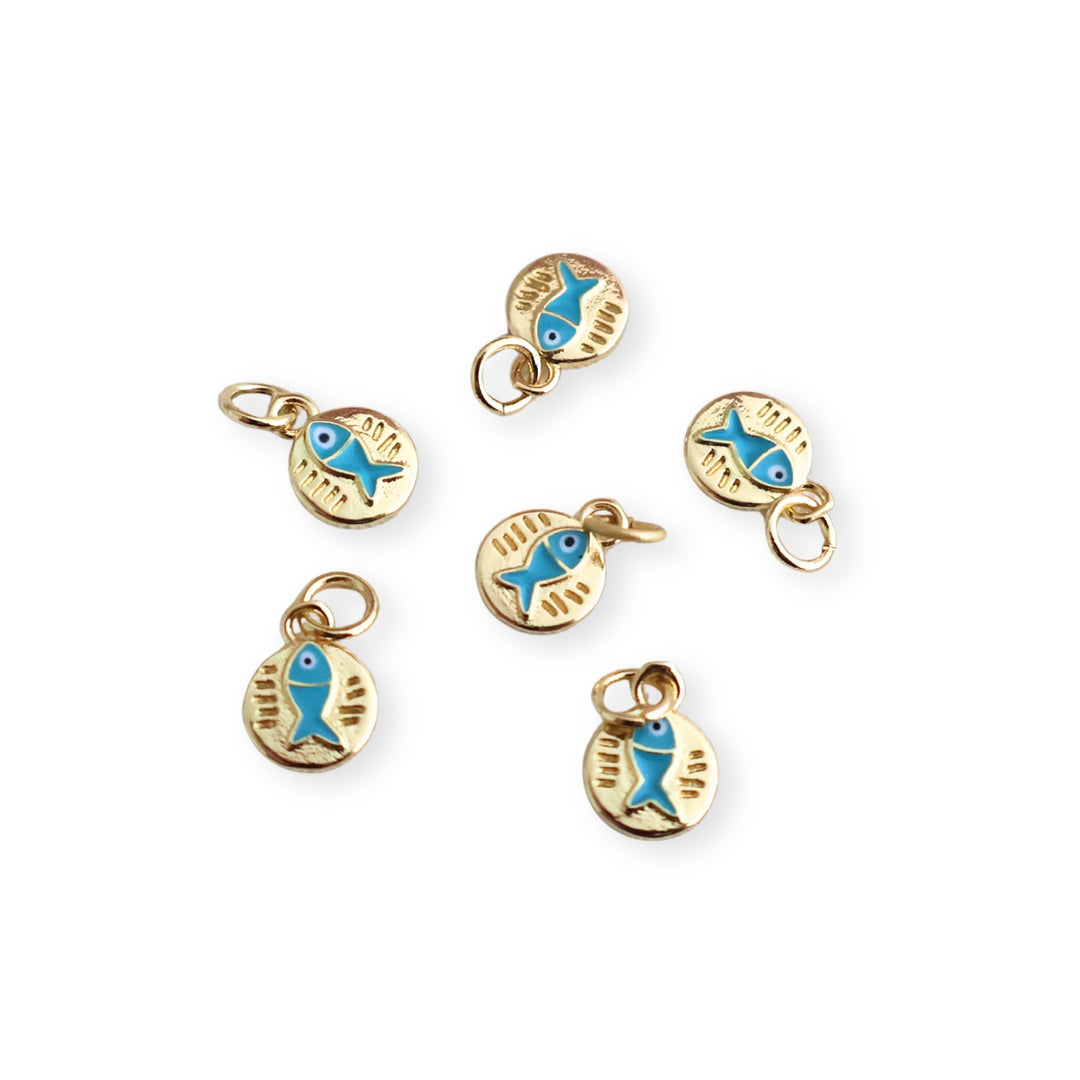 Detalle de dijes circulares de chapa de oro con pescado azul esmaltado sobre fondo blanco