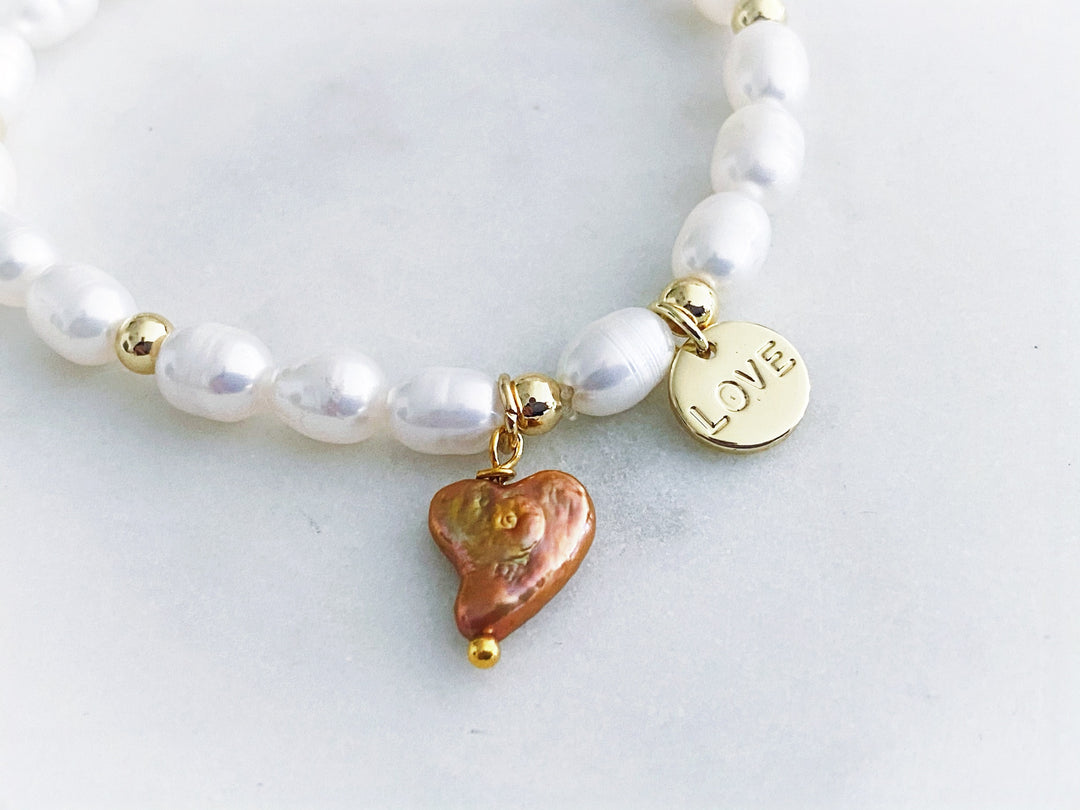 Detalle del dije "love" en chapa de oro y corazón de perla natural en la pulsera Amaré.