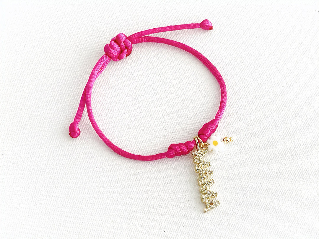 Pulsera ajustable de hilo fucsia con dije dorado “mamá” y flor metálica de murano, vista completa.