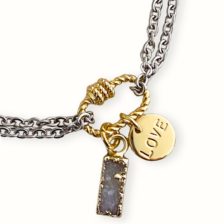 Detalle de Brazalete plateado con cadena de acero inoxidable, conector central de chapa de oro, dije Love y druzy biselado. 