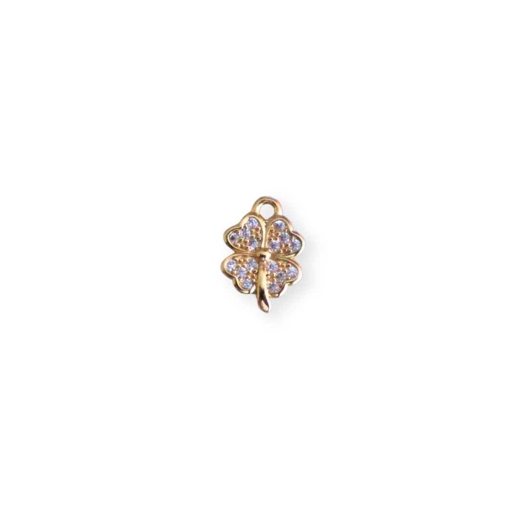 Dije dorado en forma de trébol con zirconia al centro sobre fondo claro