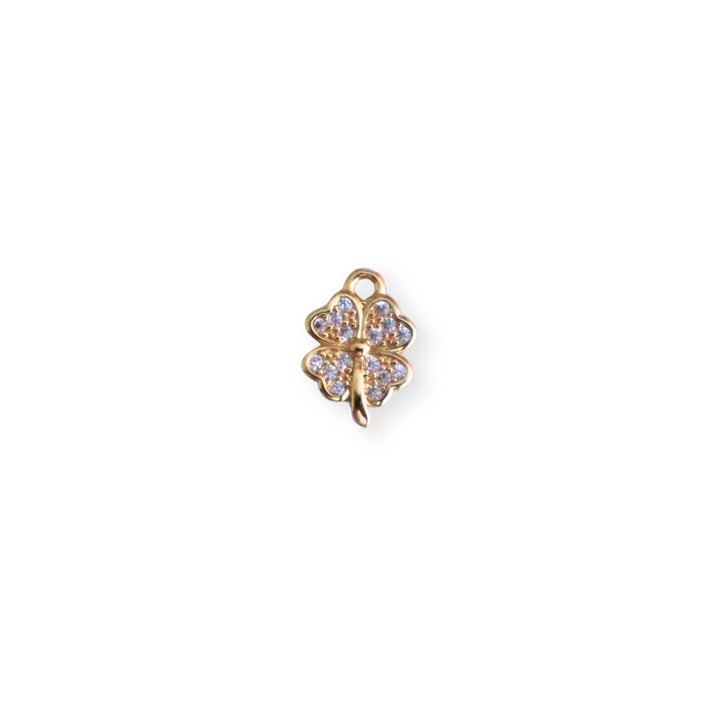 Dije dorado en forma de trébol con zirconia al centro sobre fondo claro