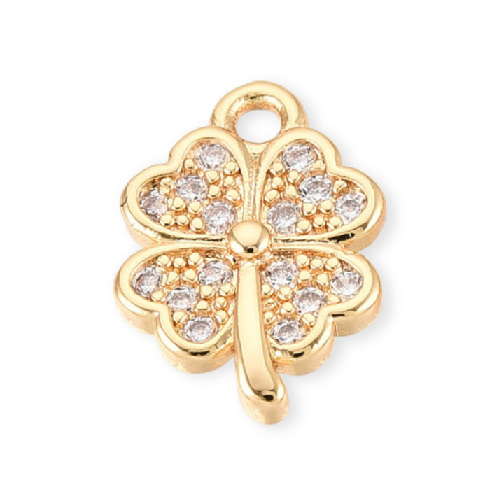 Dije dorado en forma de trébol con zirconia al centro sobre fondo claro