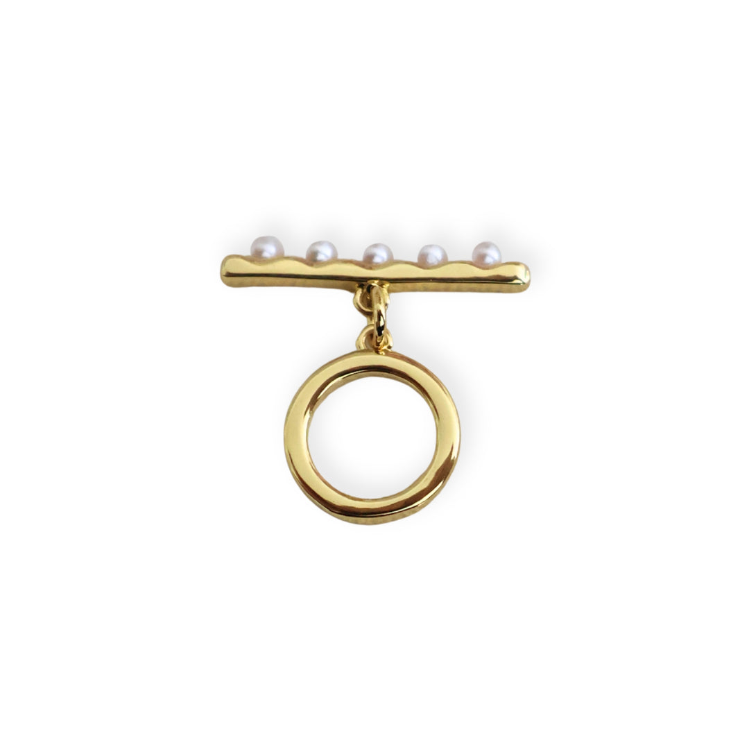 Broche tipo T de chapa de oro con perla sintética sobre fondo blanco