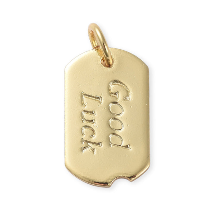 Dije plaquita dorada con grabado "Good Luck" sobre fondo blanco