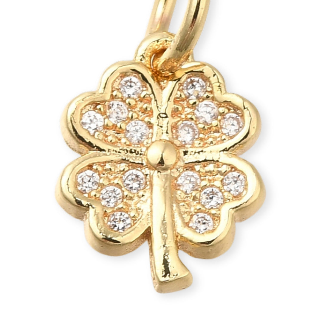 Dije en forma de trébol de chapa de oro con zirconias brillantes sobre fondo blanco