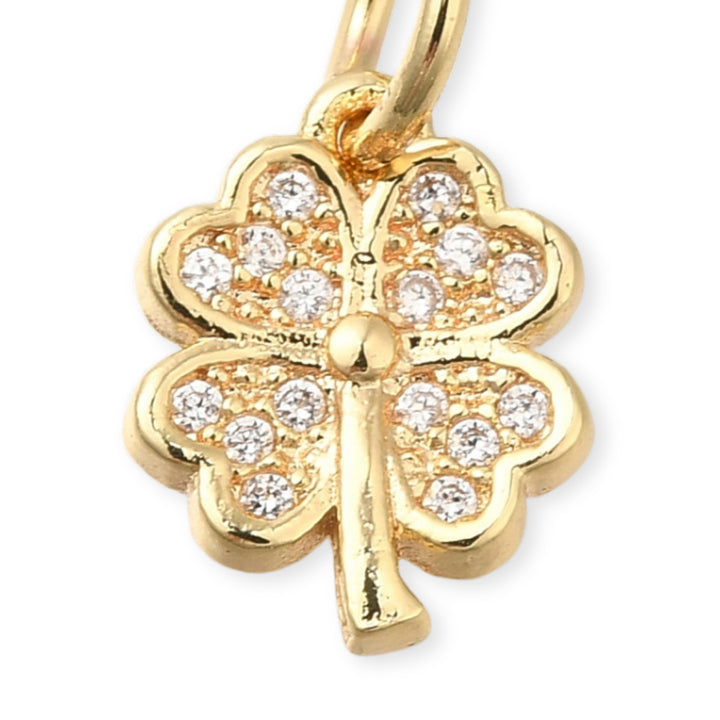 Dije en forma de trébol de chapa de oro con zirconias brillantes sobre fondo blanco