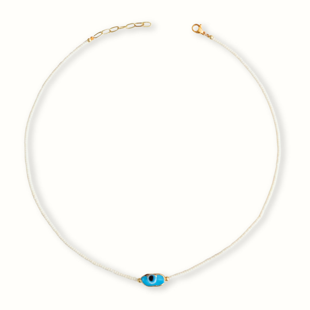 Detalle de Collar Ophia con chaquira blanca y dije de ojo en chapa de oro
