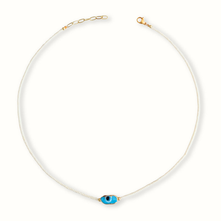 Detalle de Collar Ophia con chaquira blanca y dije de ojo en chapa de oro