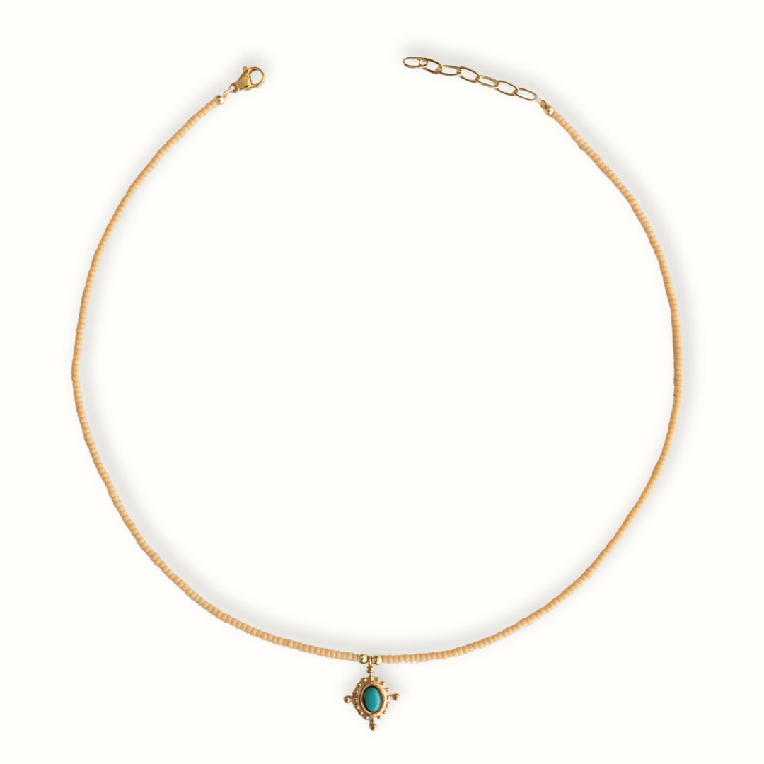 Detalle de Collar Melora con chaquira dorada y dije de cruz con piedra turquesa