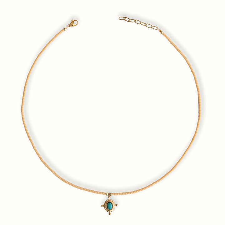 Detalle de Collar Melora con chaquira dorada y dije de cruz con piedra turquesa