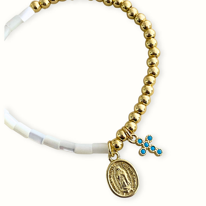 Pulsera elástica con madre perla y dijes de cruz y Virgen María en chapa de oro. 