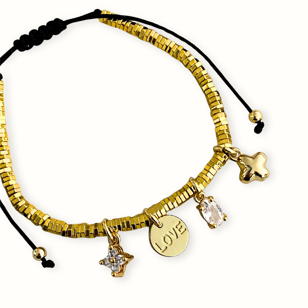Pulsera ajustable con hilo chino, hematita dorada y dijes de flor, cruz y Love en chapa de oro con zirconia.