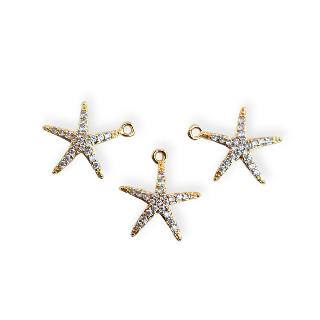 Toma a detalle de dijes de estrella de mar en chapa de oro con zirconias alrededor sobre fondo blanco