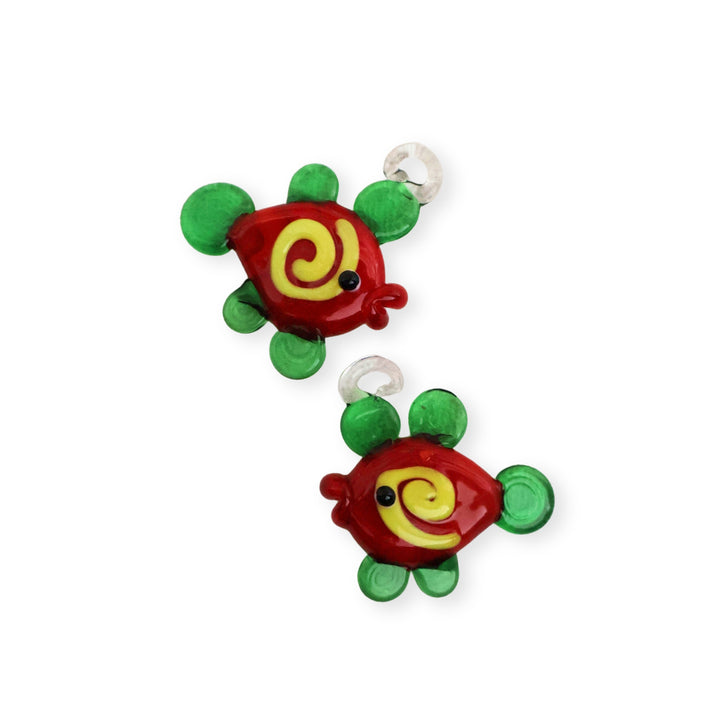 Detalles de dijes de murano en forma de pez, colores rojo oscuro y verde con espiral amarillo
