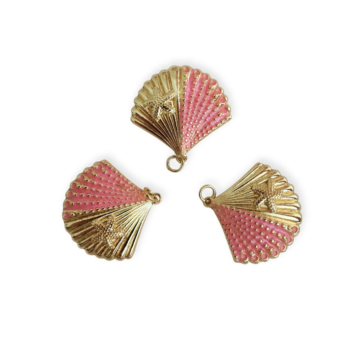 Detalle de dije en forma de concha de chapa de oro con esmalte rosa sobre fondo blanco