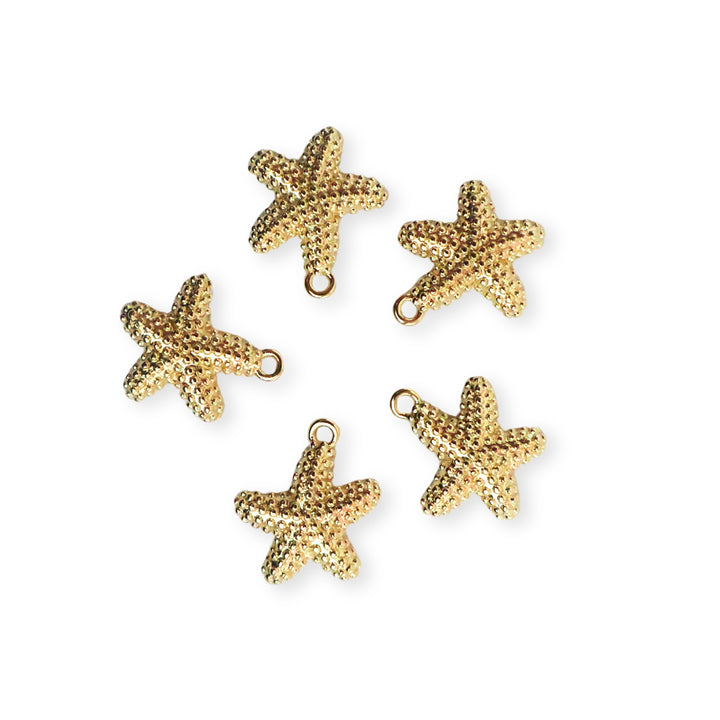 Toma a detalle de dijes de estrella de mar en chapa de oro con textura de puntos sobre fondo blanco
