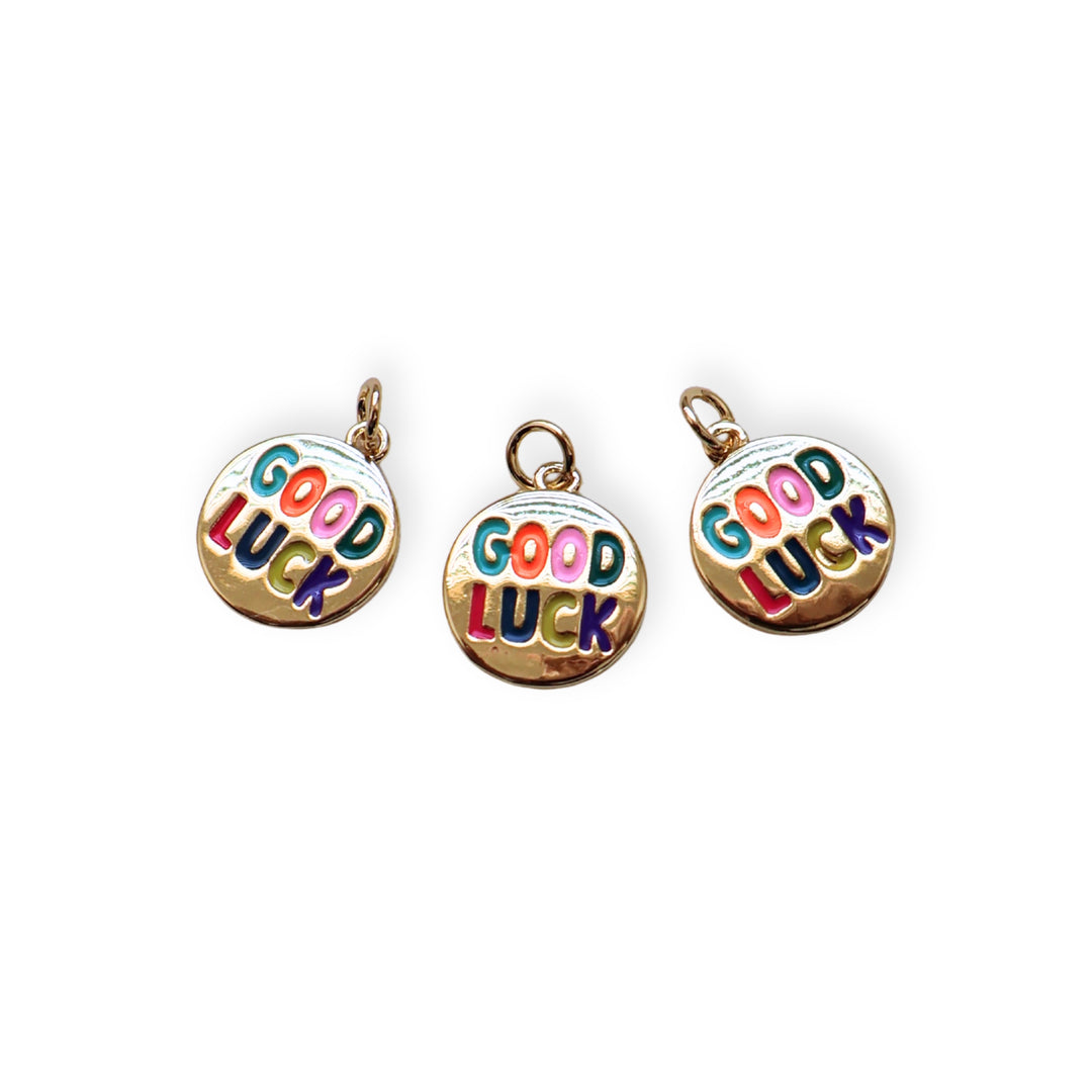 Detalles de dije circular dorado con grabado “Good Luck” y esmaltado en colores vivos