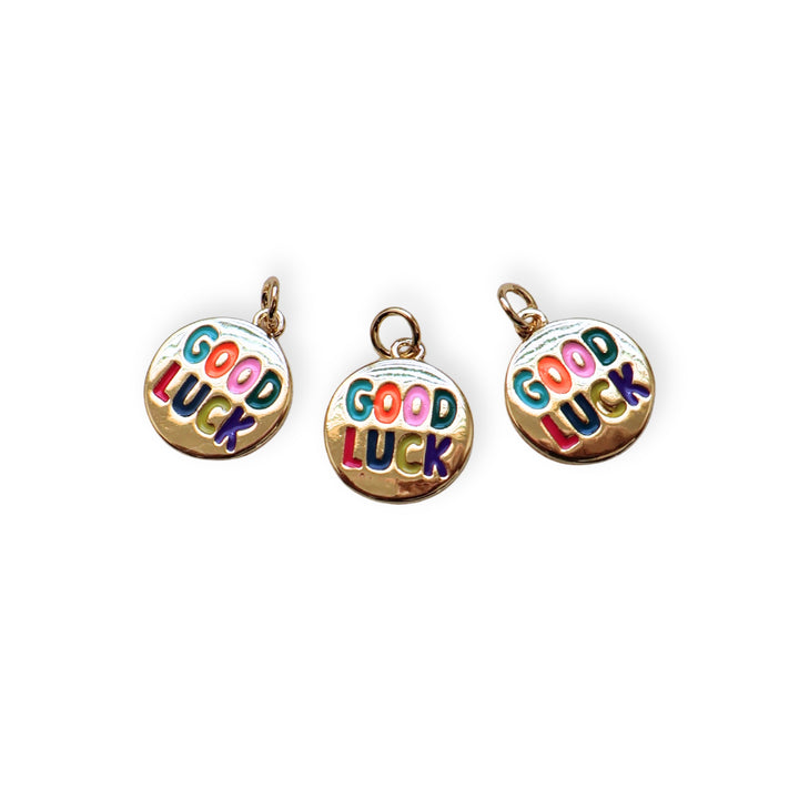 Detalles de dije circular dorado con grabado “Good Luck” y esmaltado en colores vivos