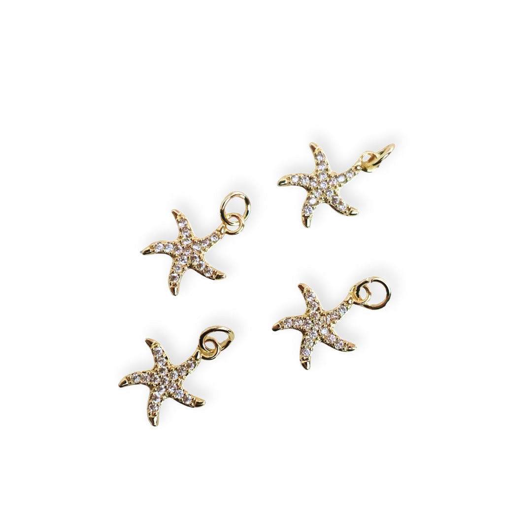 Toma a detalle para dijes de estrella de mar en chapa de oro con zirconias alrededor sobre fondo blanco