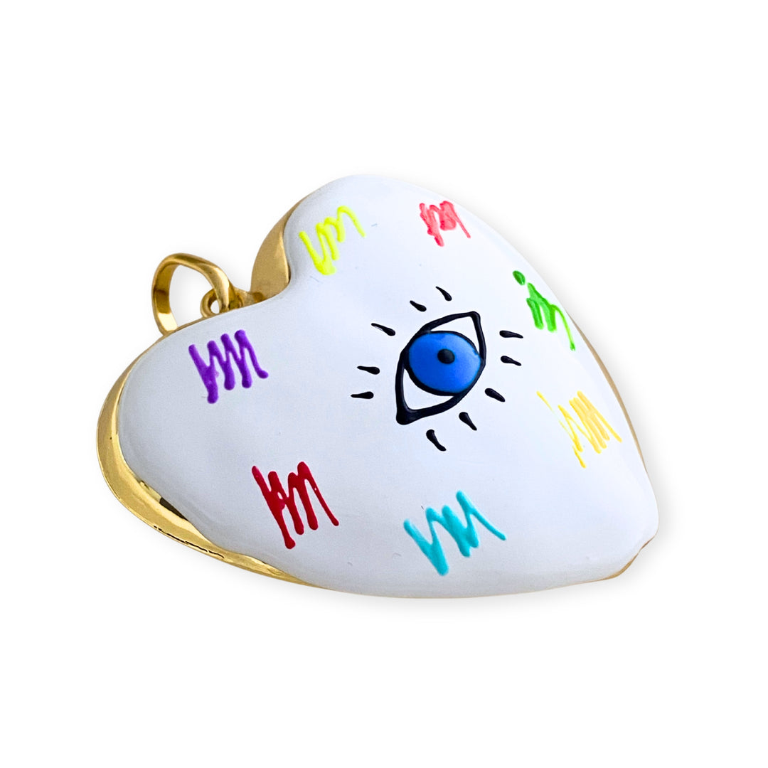 Detalles de Dije grande de corazón esmaltado blanco con ojo central y detalles multicolor en chapa de oro. 