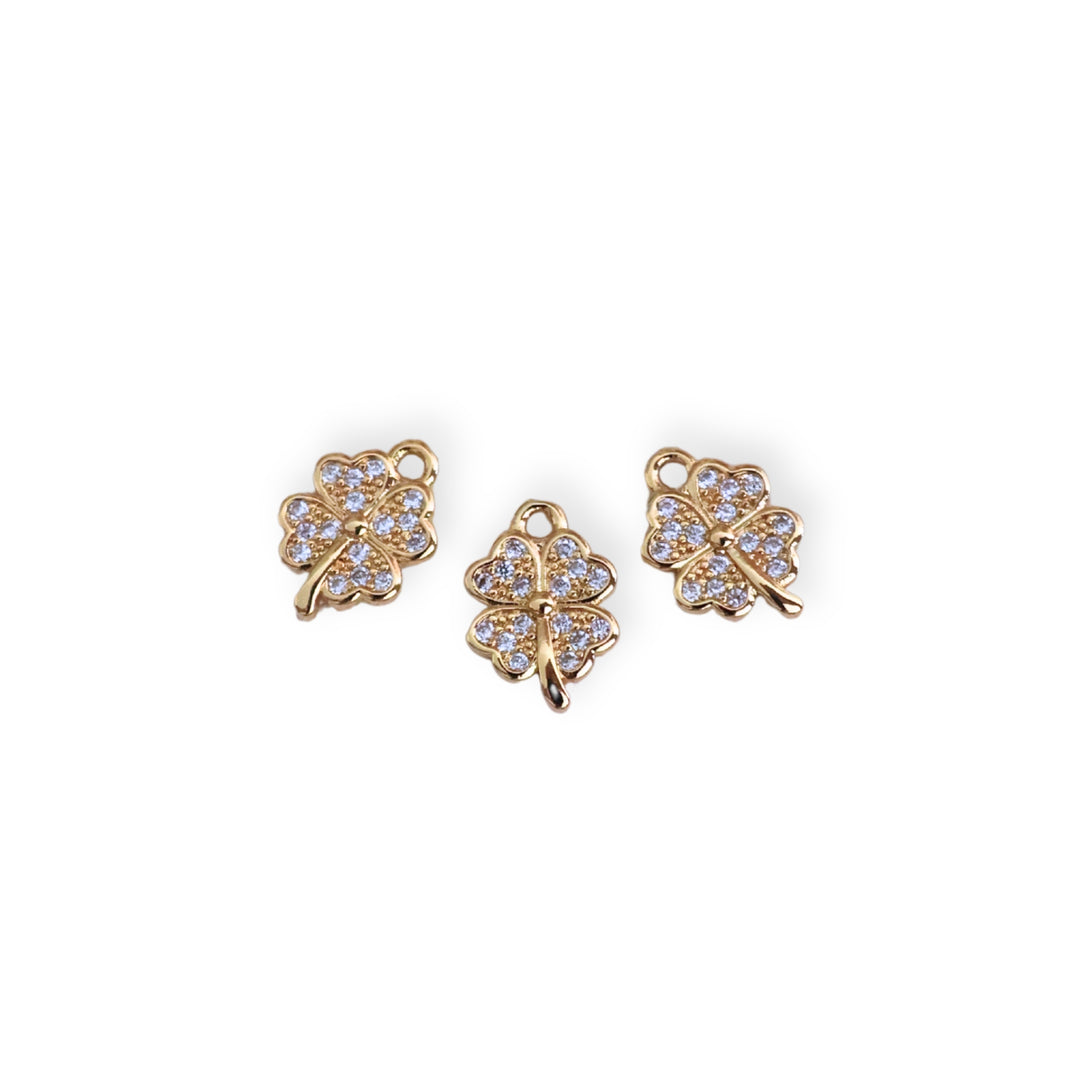 Detalles de dije dorado en forma de trébol con zirconia al centro sobre fondo claro