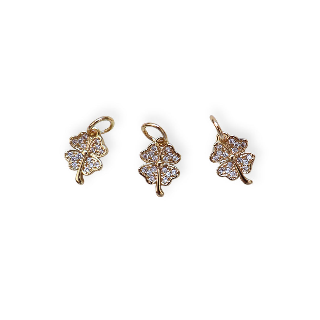 Detalles de dije en forma de trébol de chapa de oro con zirconias brillantes sobre fondo blanco