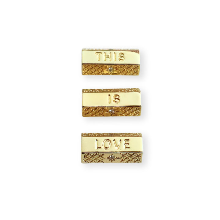 Toma a detalle de separadores de chapa de oro con grabado "THIS IS LOVE" y zirconia sobre fondo blanco