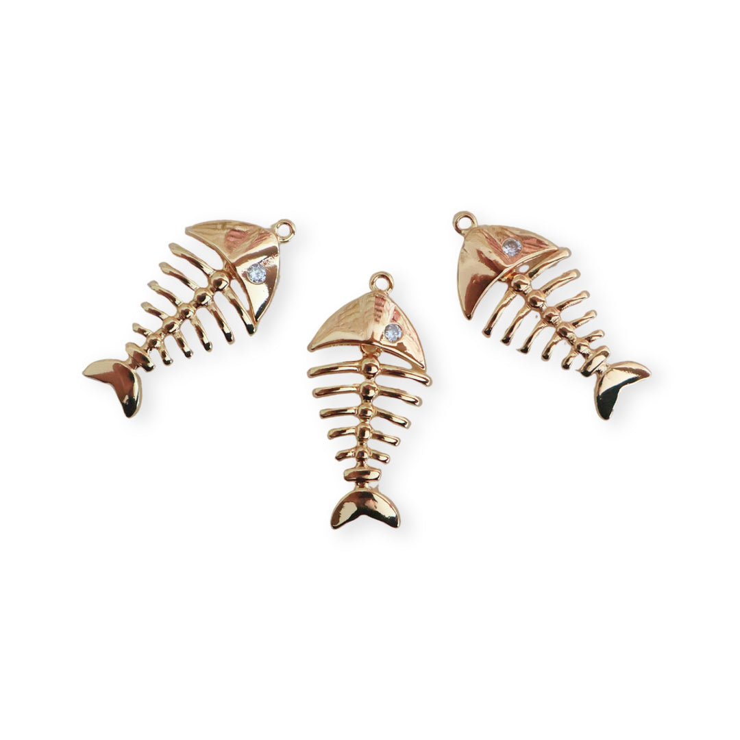 Detalle de dijes de pescado de chapa de oro con zirconia y cuerpo articulado sobre fondo blanco