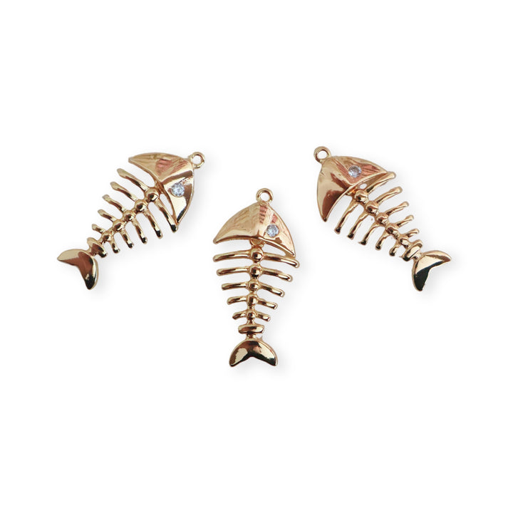 Detalle de dijes de pescado de chapa de oro con zirconia y cuerpo articulado sobre fondo blanco