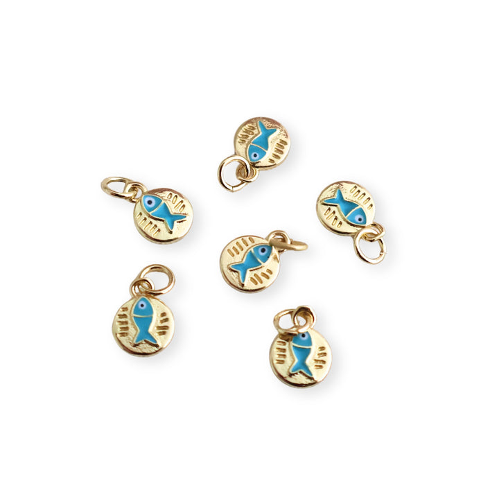 Detalle de dijes circulares de chapa de oro con pescado azul esmaltado sobre fondo blanco