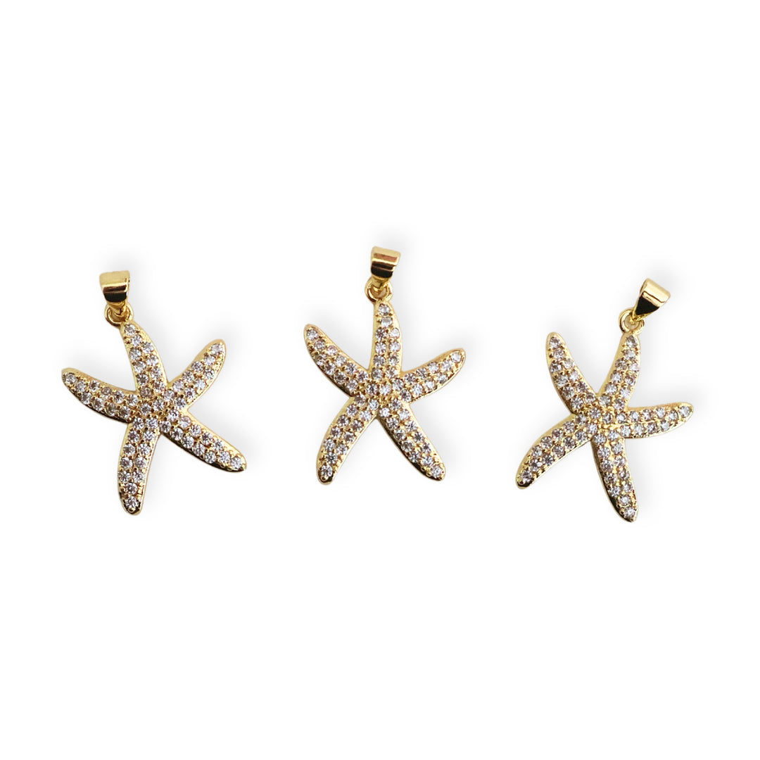 Detalle de dijes de estrella de mar en chapa de oro con zirconias sobre fondo blanco