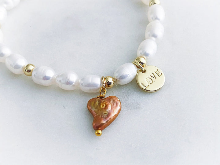 Detalle del dije "love" en chapa de oro y corazón de perla natural en la pulsera Amaré.

