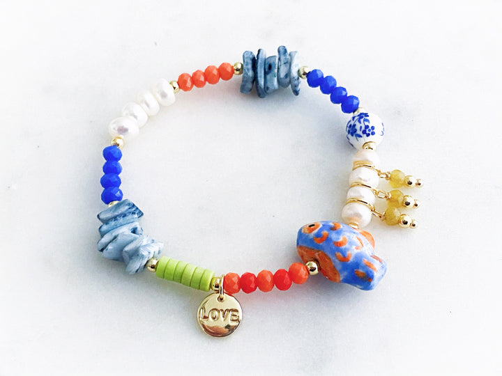 Pulsera con piedras naturales, perlas y cristales, decorada con dijes de concha, pez y placa “love”, vista completa.