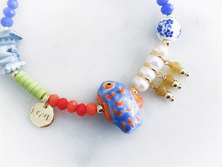 Detalle del dije de concha natural y pez de cerámica en la pulsera con piedras y perlas.