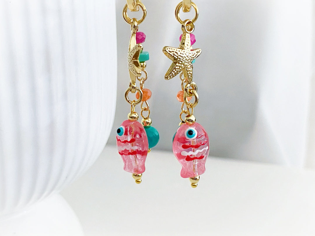 Detalle de piedras en tonos rosa, naranja y azul con estrella dorada y dije de pez