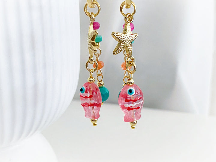Detalle de piedras en tonos rosa, naranja y azul con estrella dorada y dije de pez