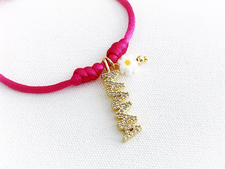 Detalle de pulsera ajustable de hilo fucsia con dije dorado “mamá” y flor metálica de murano, vista completa.