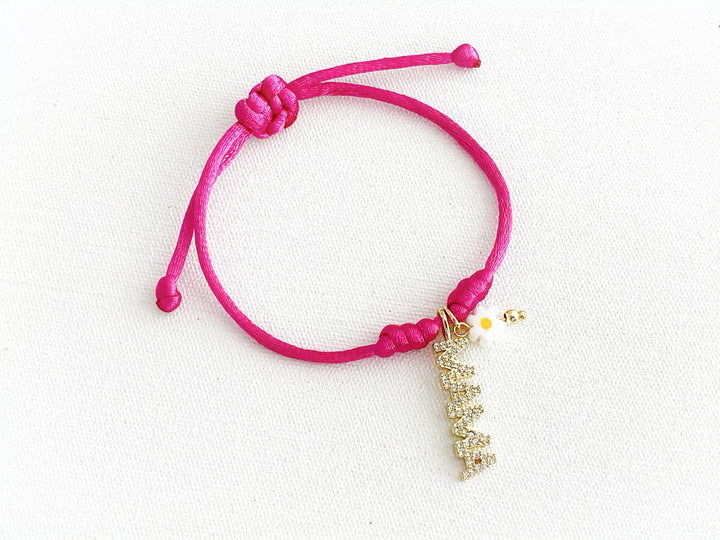 Pulsera ajustable de hilo fucsia con dije dorado “mamá” y flor metálica de murano, vista completa.